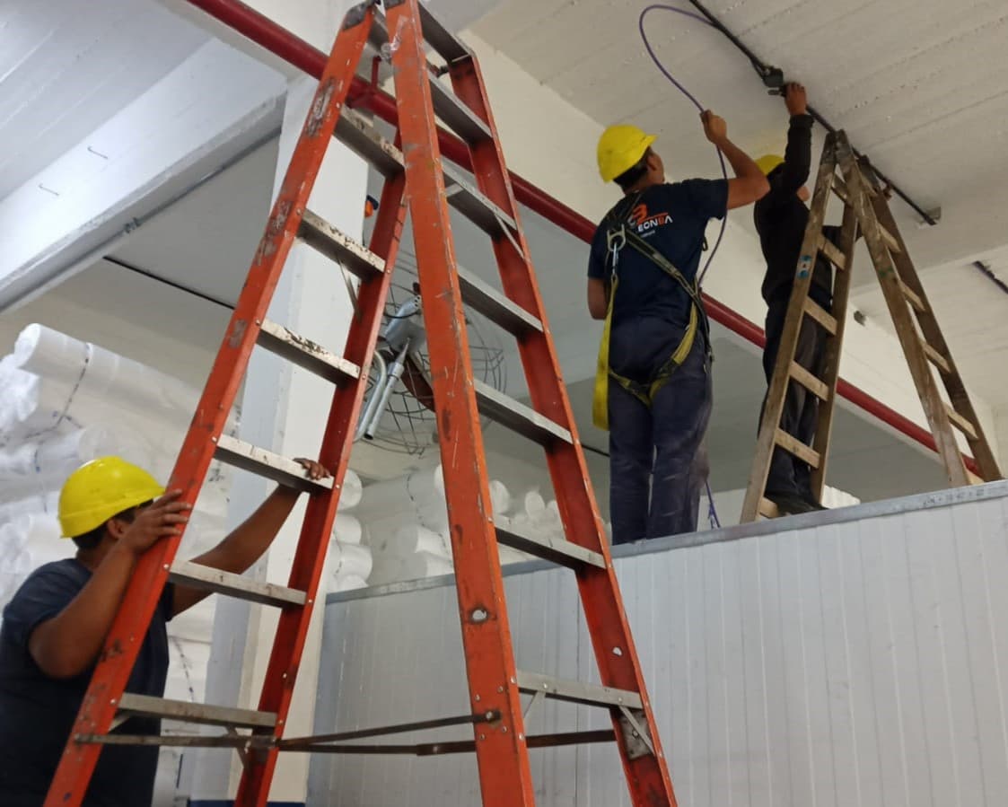 Trabajadores en escaleras haciendo una instalación eléctrica.